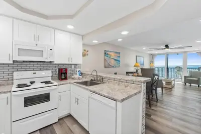 a kitchen with white appliances and a living room at Pelican Walk 703 in Panama City Beach