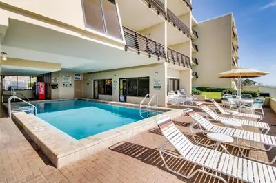 a swimming pool with chairs and a table and a building at Gulfgate 102 in Panama City Beach