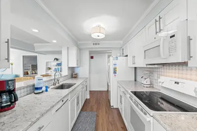 a white kitchen with marble counter tops and white cabinets at Pelican Walk 1008 in Panama City Beach