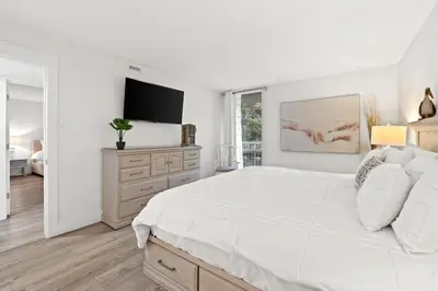 a white bedroom with a large bed and a flat screen tv at Pelican Walk 207 in Panama City Beach