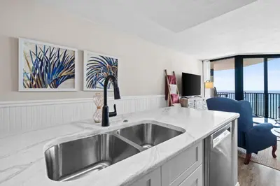 a kitchen with a stainless steel sink and a living room at Sunbird Beach Resort 1011W By Book That Condo in Panama City Beach