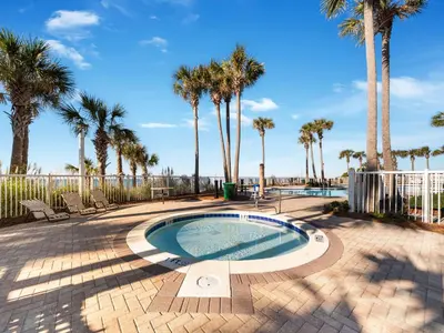 a swimming pool with palm trees and a fence at Grand Panama Beach Resort - The Grand II #803 in Panama City Beach