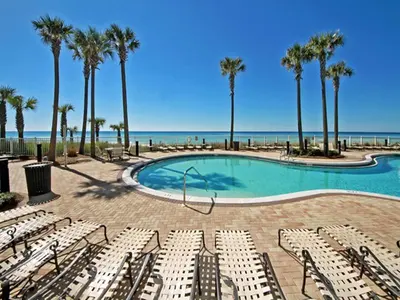 a pool with chairs and palm trees and the ocean at Grand Panama Beach Resort - The Grand II #803 in Panama City Beach
