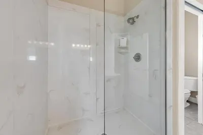 a white bathroom with a shower with a glass door at Relax Awhile - Main House in Panama City Beach