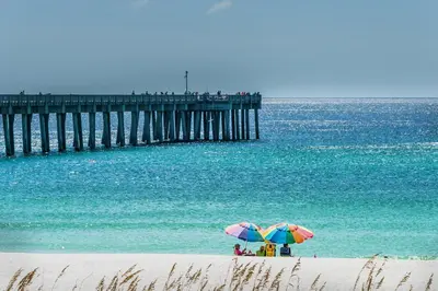 two people under umbrellas on a beach near a pier at Calypso 2-103 West in Panama City Beach