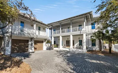 an exterior view of a white house with a driveway at 94 Pinecrest by Oversee 30A in Inlet Beach