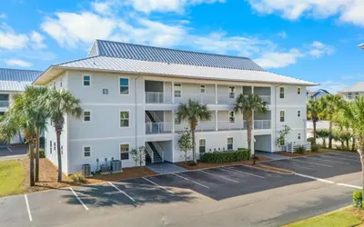 an apartment building with palm trees in a parking lot at Aqua Bella by Oversee 30A in Santa Rosa Beach