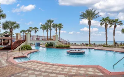a pool with palm trees and a boat in the water at Shores of Panama Chic 2-BD Beachfront Resort Condo! by Dolce Vita Getaways! in Panama City Beach