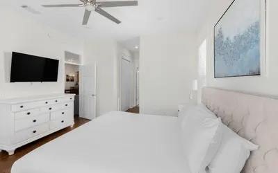 a white bedroom with a bed and a flat screen tv at Beach Dreamer by Oversee 30A in Seacrest