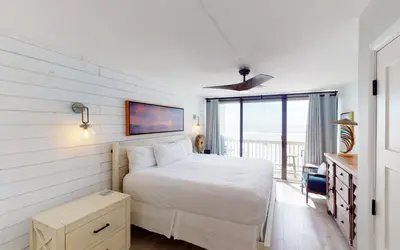 a bedroom with a white bed and a balcony at Beach Pleeze by Oversee 30A in Panama City Beach