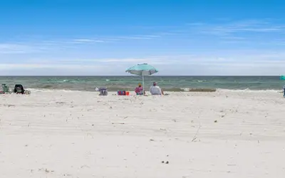 two people sitting under an umbrella on the beach at Beachfront Oasis by Oversee 30A in Panama City Beach