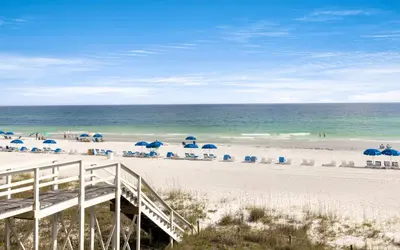 a beach with blue umbrellas and chairs and the ocean at Peaceful Easy Feeling by Oversee 30A in Carillon Beach