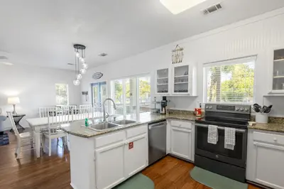 a kitchen with white cabinets and a sink and a table at Coral Reef by Oversee 30A in Santa Rosa Beach