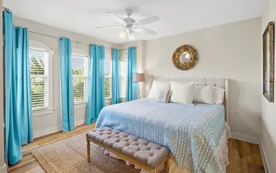 a bedroom with a bed with blue curtains and a fan at Oasis By The Water by Oversee 30A in Seacrest