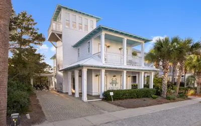 a white house with a balcony and palm trees at The Loopy Crab by Oversee 30A in Seacrest