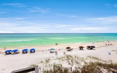 a beach with blue umbrellas and people on the beach at Into the Mystic by Oversee 30A in Seacrest
