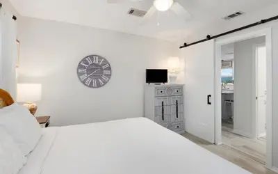 a white bedroom with a bed and a clock on the wall at Noras Place by Oversee 30A in Santa Rosa Beach