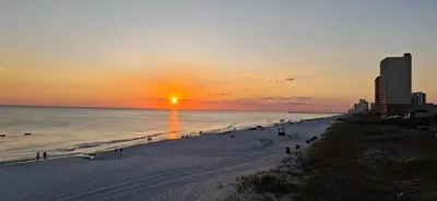 a beach at sunset with the sun setting over the ocean at ON THE BEACH! COUPLES GETAWAY,HONEYMOON SWEET, Perfectly Cozy Beach Front Condo, full kitchen, pool, free parking,CHECK-IN AT DOOR in Panama City Beach
