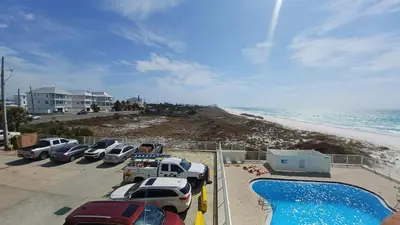 a parking lot with cars parked next to the beach at ON THE BEACH! COUPLES GETAWAY,HONEYMOON SWEET, Perfectly Cozy Beach Front Condo, full kitchen, pool, free parking,CHECK-IN AT DOOR in Panama City Beach