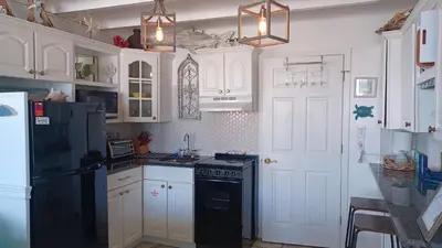 a kitchen with white cabinets and a black refrigerator at ON THE BEACH! COUPLES GETAWAY,HONEYMOON SWEET, Perfectly Cozy Beach Front Condo, full kitchen, pool, free parking,CHECK-IN AT DOOR in Panama City Beach