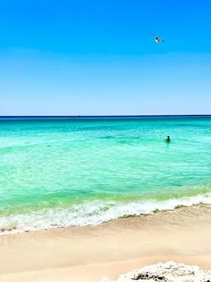 a person swimming in the ocean on a beach at Lets Get You Laguna Beachin in this Brand New Cottage Steps to the Beach in Panama City Beach