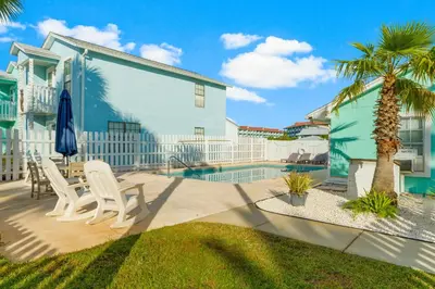 a patio with chairs and a palm tree and a pool at Sand Castle West #G6 in Panama City Beach