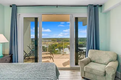 a bedroom with a bed and a chair and a balcony at Laketown Wharf #1034 in Panama City Beach