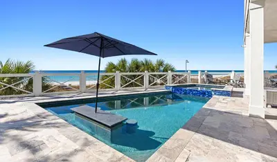 a swimming pool with an umbrella and the ocean at Sunset Serenity in Panama City Beach