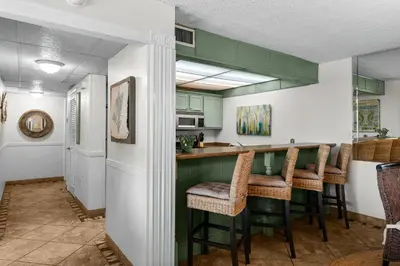 a kitchen with green cabinets and bar stools at Moondrifter #803 in Panama City Beach