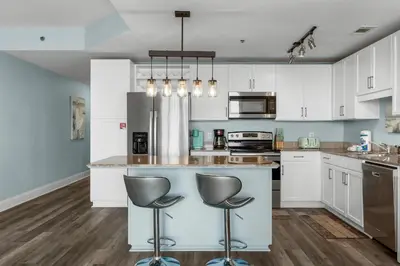 a kitchen with white cabinets and a island with two bar stools at Spectacular Ocean View Condo! Steps to the Beach! by Dolce Vita Getaways PCB! in Panama City Beach