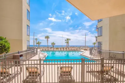 a swimming pool with chairs and the ocean in the background at Sunbird Beach Resort #604 East in Panama City Beach