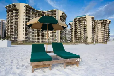 two chairs and an umbrella on the beach with buildings at Sunbird Beach Resort #604 East in Panama City Beach