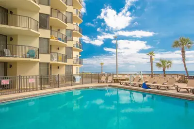 a swimming pool in front of a hotel with chairs and the ocean at Sunbird Beach Resort #604 East in Panama City Beach