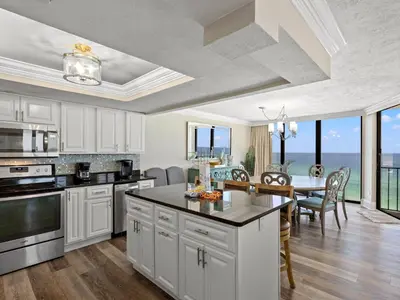 a kitchen with white cabinets and a dining room with a table at Edgewater Tower III #1212 in Panama City Beach