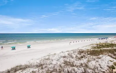 a beach with umbrellas and people walking on it at Seashell Castle by Oversee 30A in Santa Rosa Beach