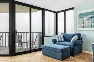a living room with a blue chair and a balcony at Ocean Front Beach Condo in Panama City Beach