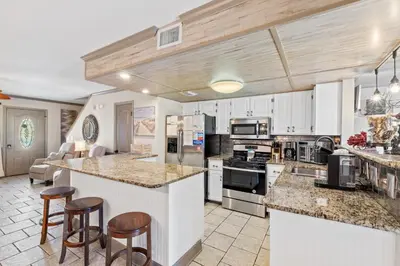 a large kitchen with white cabinets and bar stools at Coconut Cottage in Panama City Beach