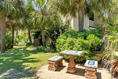 a table and two stools in a yard with palm trees at Coconut Cottage in Panama City Beach