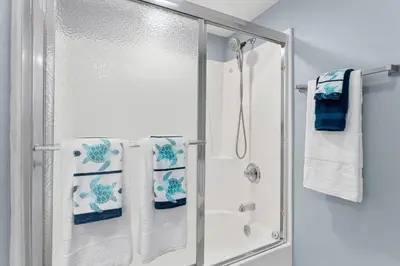 a bathroom with a shower and a sink with towels at Sandpiper Beacon Beach Resort in Panama City Beach