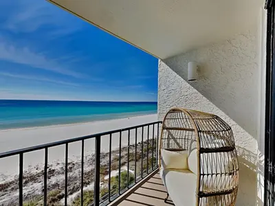 a rattan chair sits on a balcony overlooking the beach at Edgewater Tower III #708 in Panama City Beach