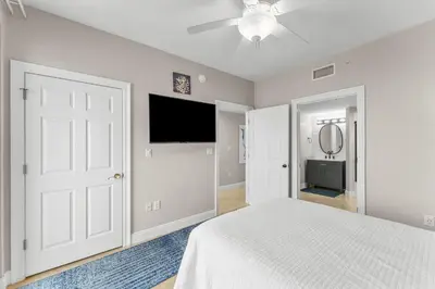 a white bedroom with a bed and a flat screen tv at Treasure Island #1401 in Panama City Beach