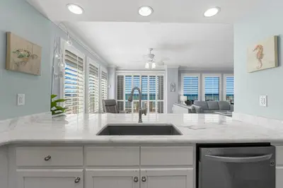 a white kitchen with a sink and a living room at Treasure Island #0101 in Panama City Beach