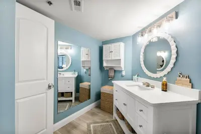 a bathroom with blue walls and a white sink and mirror at Sunbird 107E by InJoy Vacations in Panama City Beach