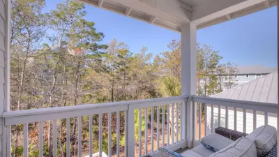 a balcony with a couch and a view of the woods at Coconut Cove by AvantStay Deck w Hot Tub Access to 2 Pools in Santa Rosa Beach