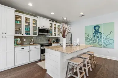 a kitchen with white cabinets and a island with stools at 6-Seater Golf Cart - Community Pool - Close to Beach, Dining and Shopping in Inlet Beach