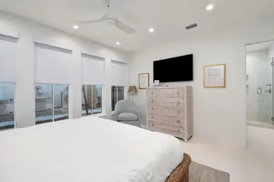 a white bedroom with a bed and a flat screen tv at Selah at the Sea in Santa Rosa Beach