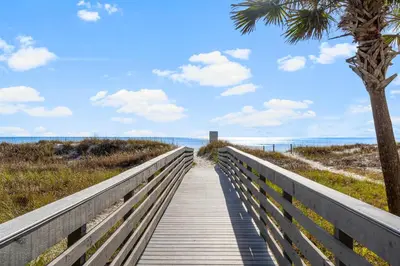 a boardwalk to the beach with a palm tree at Salt Life Bungalow in Panama City Beach