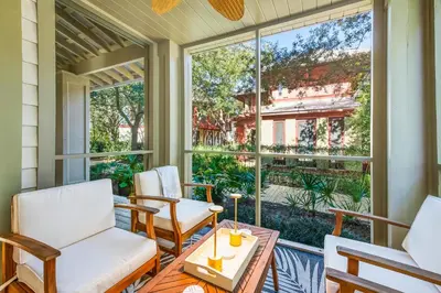 a porch with white chairs and a table and windows at Captain Jack Cottage in Rosemary Beach
