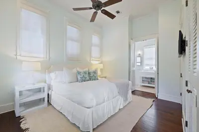 a white bedroom with a bed and a ceiling fan at PTO Cottage in Rosemary Beach