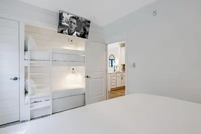 a white bedroom with a bed and a tv at Percy's Flat in Rosemary Beach